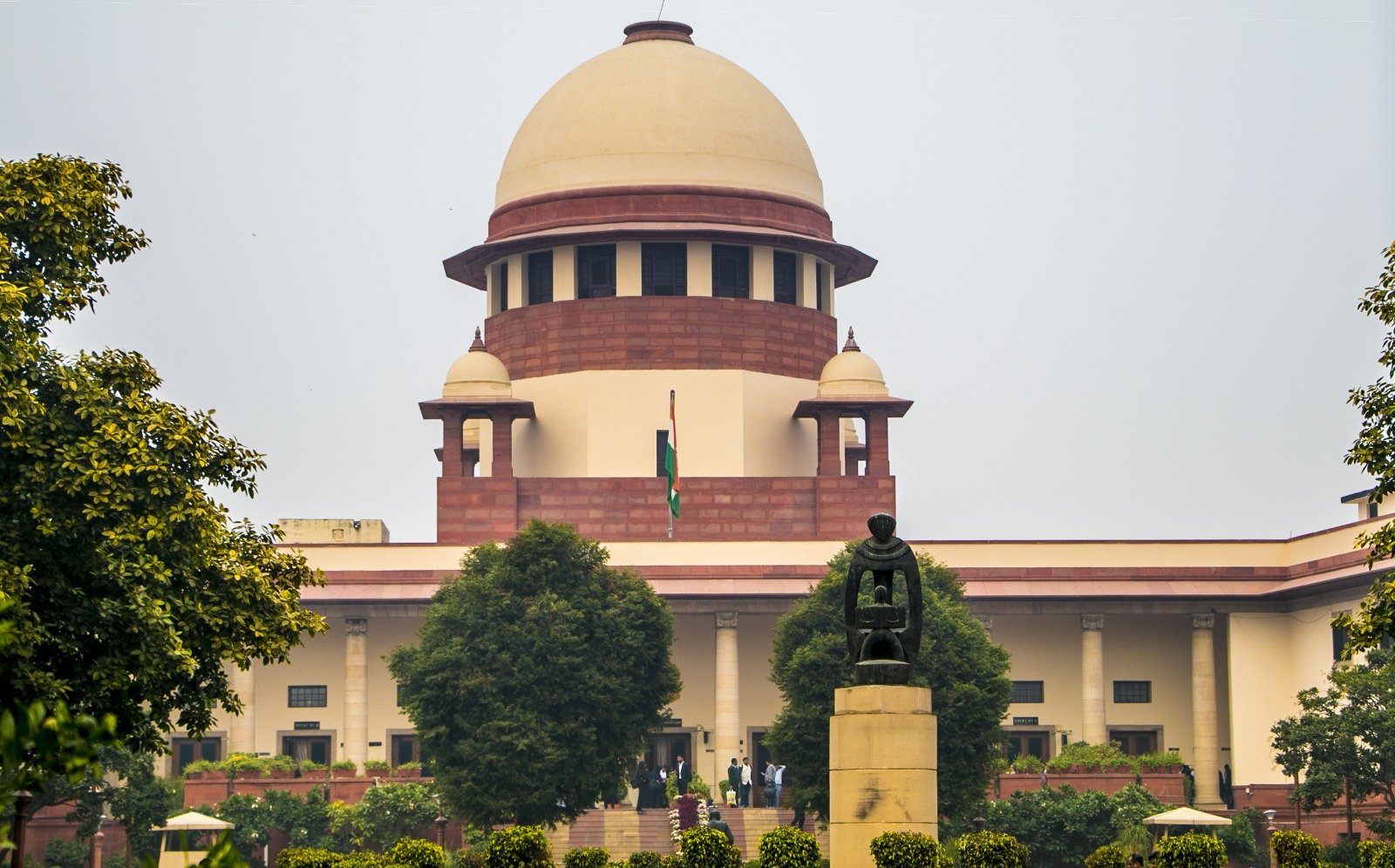 Exterior view of the Supreme Court of India building in New Delhi, featuring its iconic central dome, landscaped gardens, and Indian national flag.
