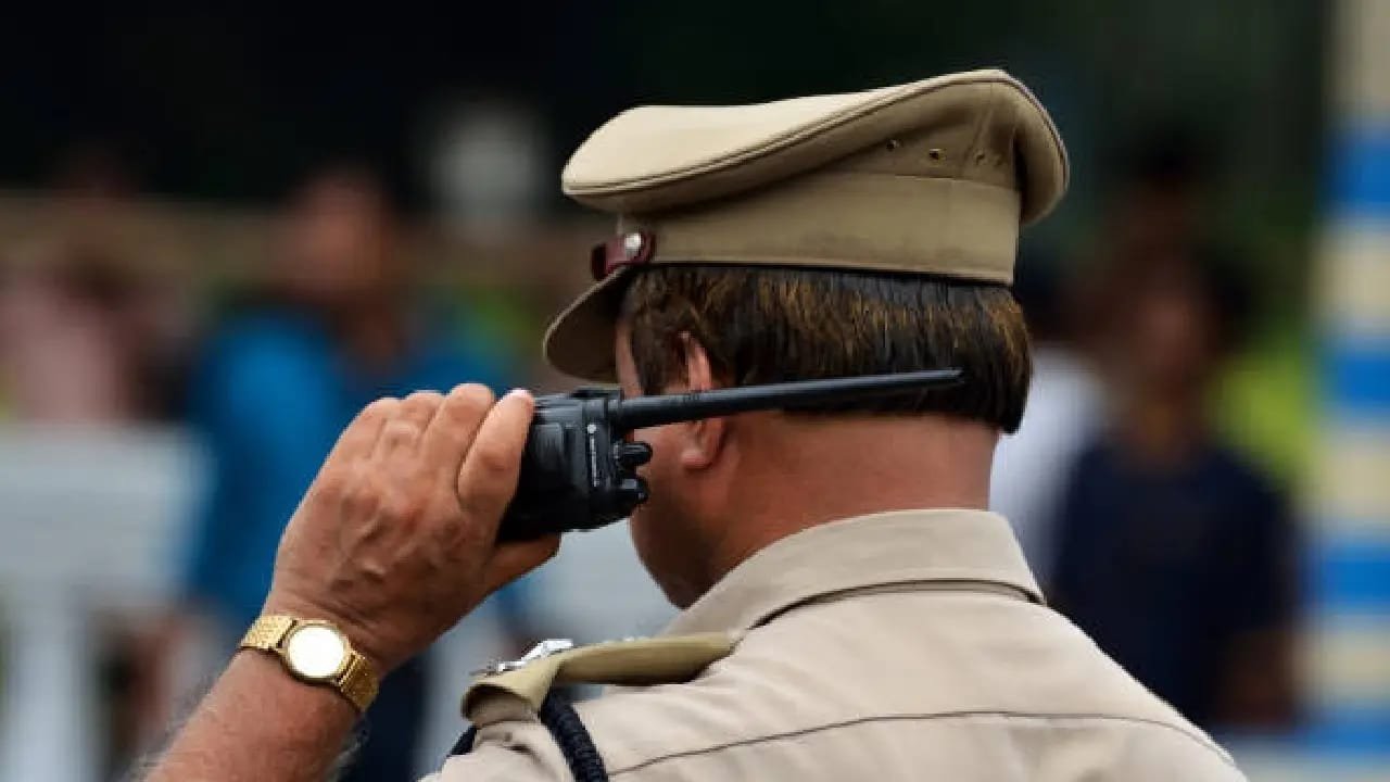 A uniformed police officer wearing a khaki cap salutes while standing in a public area.