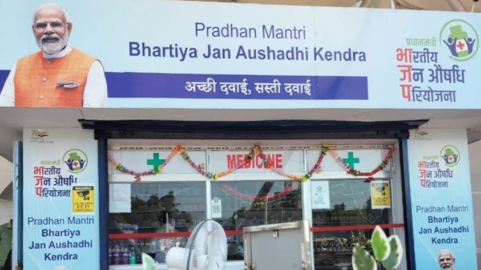 Storefront of Pradhan Mantri Bhartiya Jan Aushadhi Kendra with signboard saying "Acchi Dawai, Sasti Dawai" and Medicine shop decorated with garlands.