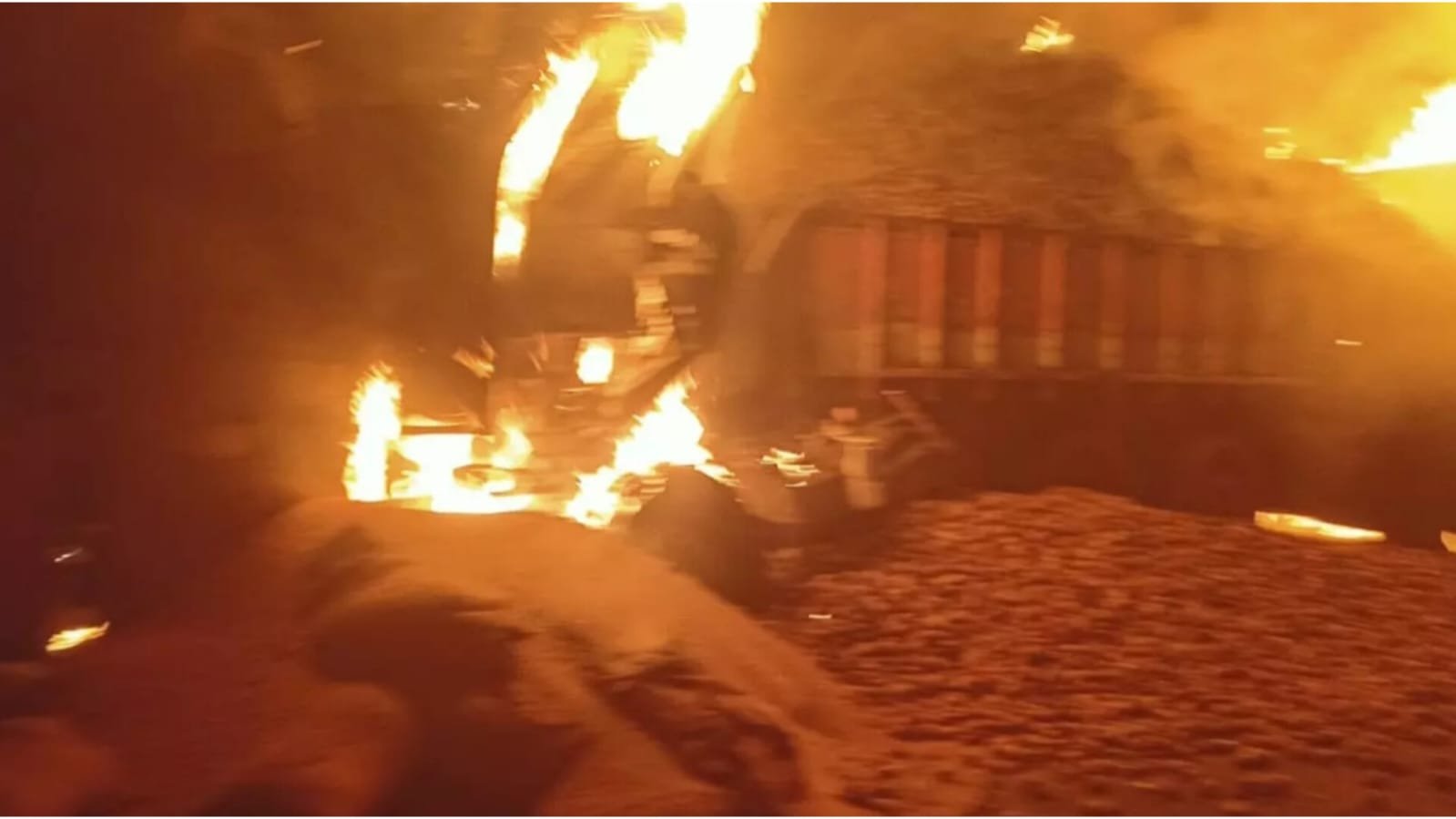 Several trucks engulfed in flames at night, with towering fire and thick smoke spreading across the scene.