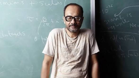 Man in glasses standing in front of chalkboard with equations.