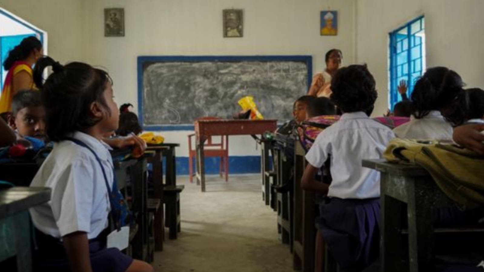 Students sitting in a classroom with teachers near blackboard.
