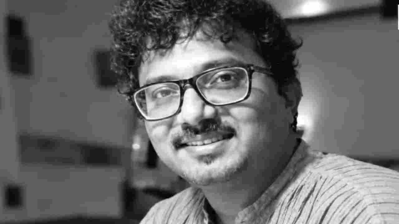 Black and white portrait of a smiling man with curly hair, moustache and glasses, wearing a striped kurta.